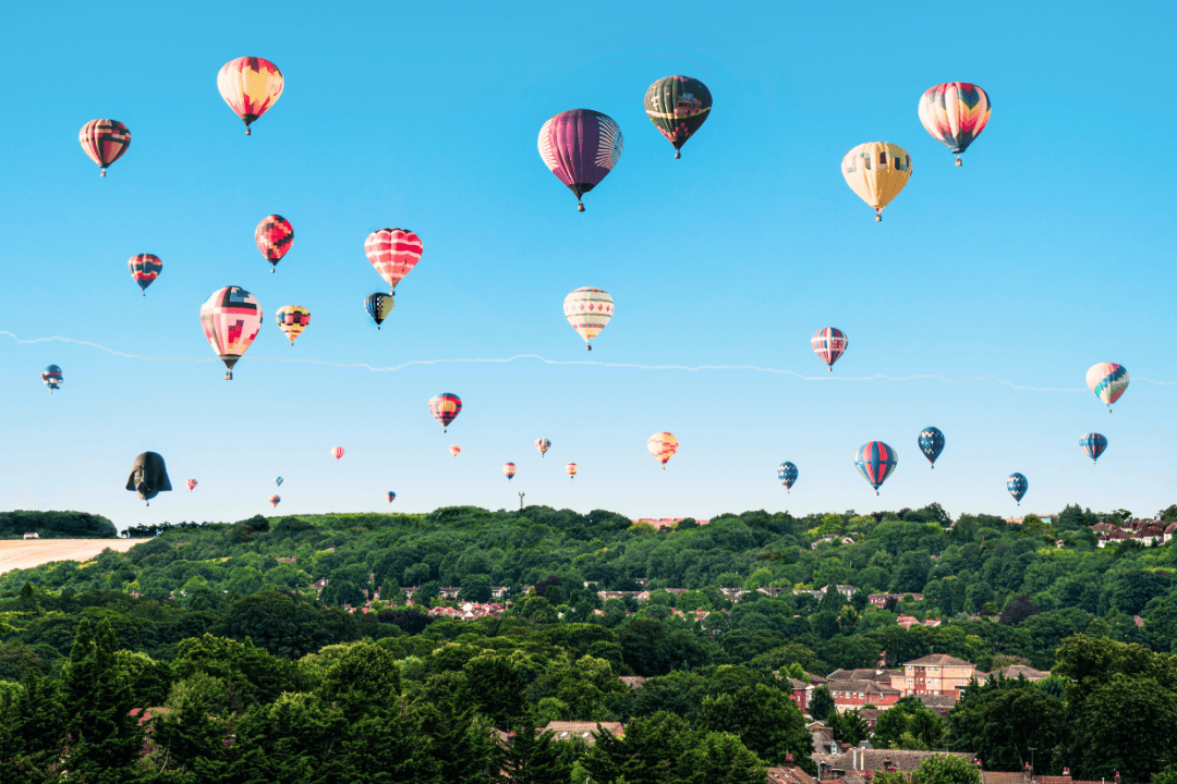 Ein Foto von 33 bunten Heißluftballons an einem strahlend blauen Himmel über einem Wald aus kräftig grünen Bäumen
