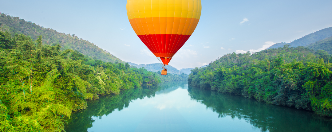 Foto eines farbenprächtigen Heißluftballons, der über einem Fluß schwebt